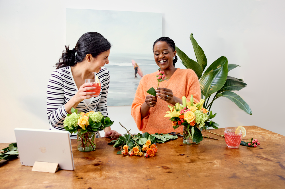 Two people designing bouqets and drinking cocktails while following an Alice's Table Virtual Workshop on a tablet