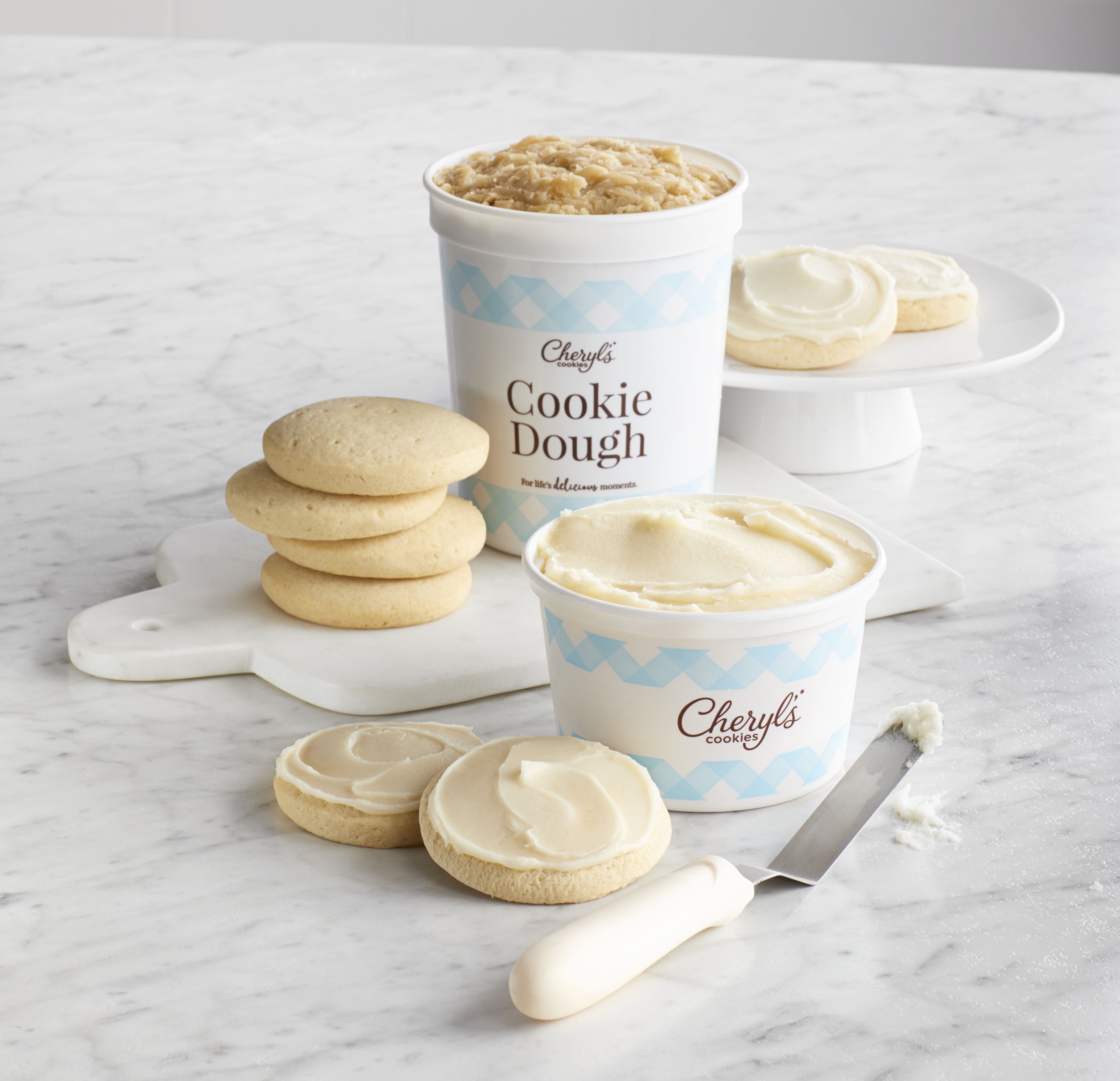 A display of Cheryl's Cookies Cut-out Cookie Dough and Buttercream Frosting Set on a white platter placed on  a white-marbled countertop