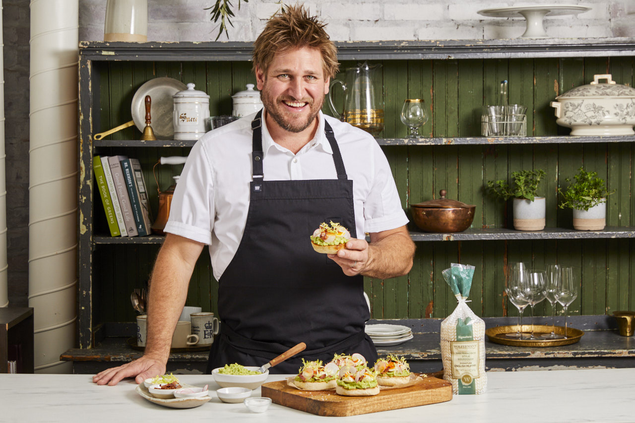 Chef Curtis Stone behind a kitchen counter with his avacado toast creation featuring a Wolferman's Bakery English Muffin