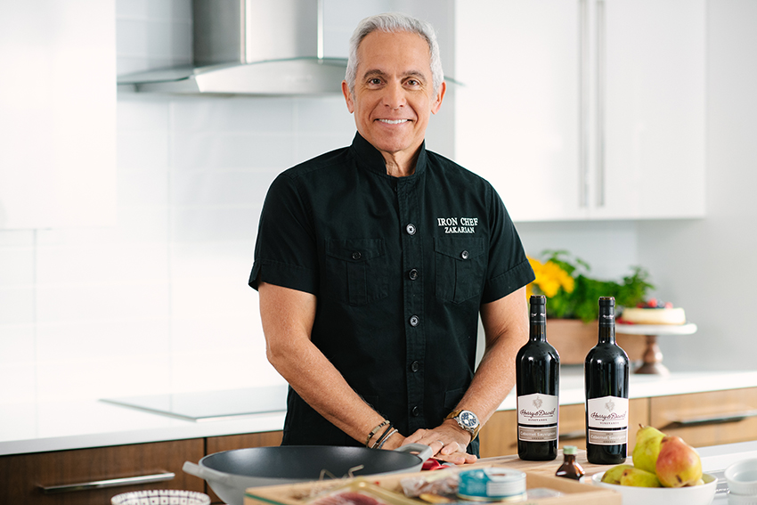 Chef Geoffrey Zakarian in front of a kitchen counter next to Harry and David wine and pears