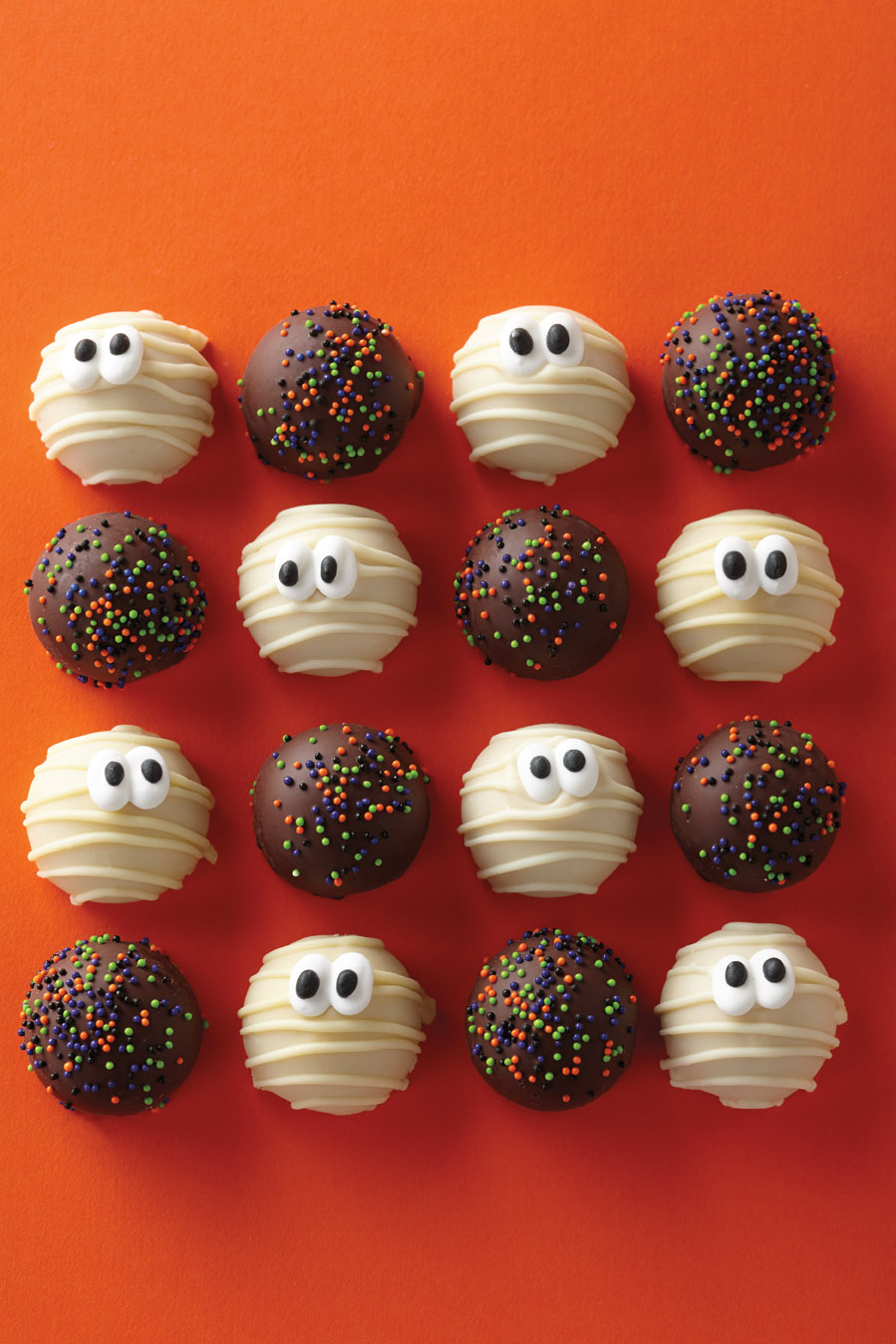 Four rows of alternating mummy themed and chocolate Harry & David Cake Pops decorated for Halloween on an orange background