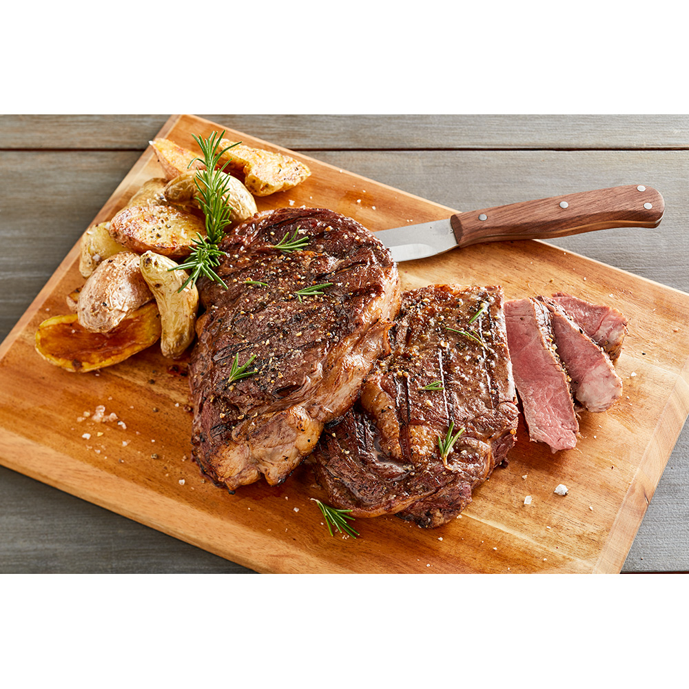 A cooked ribeye steak from Harry and David on a cutting board with roasted potatoes