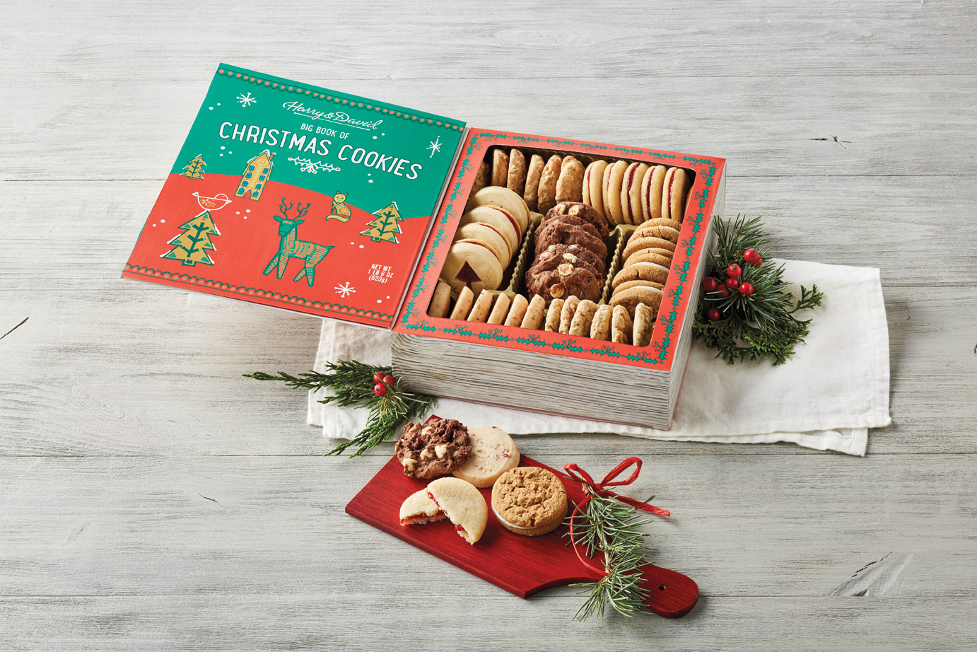 A display of the Harry and David Big Book of Christmas Cookies product, decorated with holly and evergreen branches