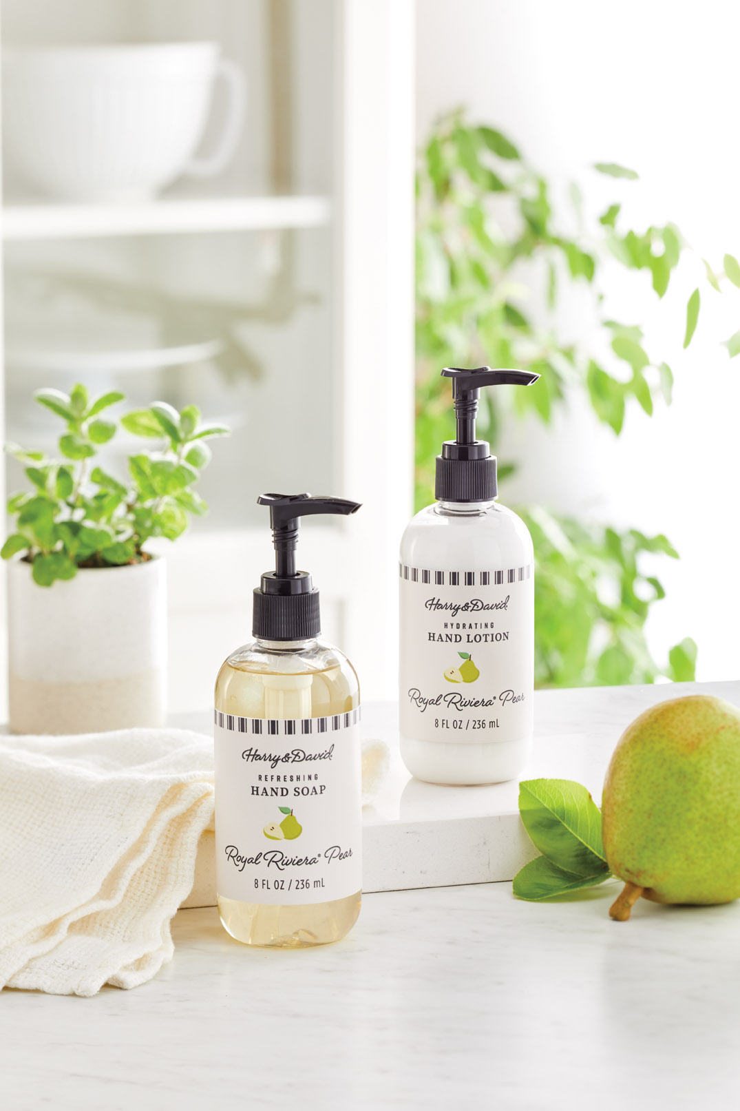 Harry & David Royal Riviera Pears scented hand soap and lotion displayed on a white counter decorated with greenery, a pear, and a hand towel