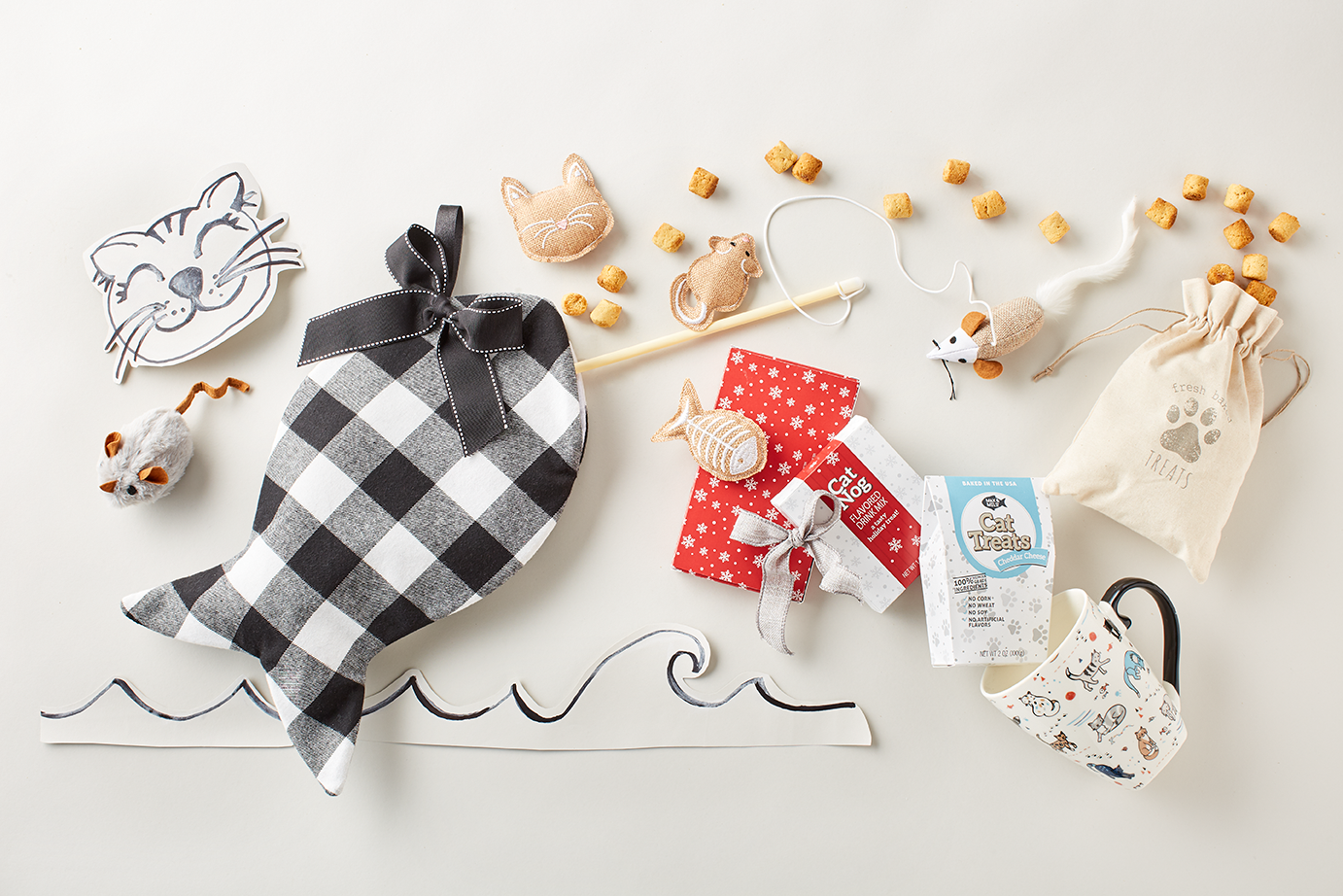 A spread of Max & Milo Holiday Cat Stocking items including a gingham, fish-shaped toy, cat treats, cat and mouse plushes, and a cat-decorated mug