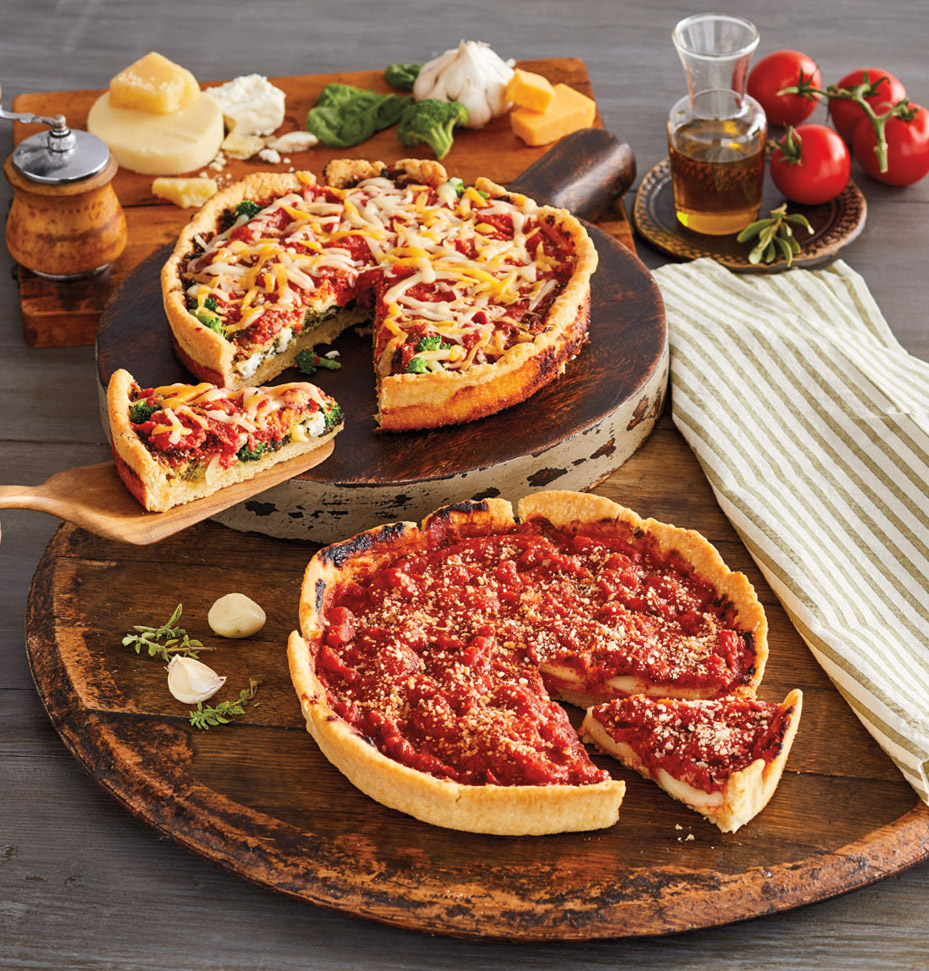 A display of the Pizzeria Uno Veggie Lover's Deep-Dish Pizza 2-Pack on wooden platters and garnished with tomatoes, cheese, olive oil, and garlic