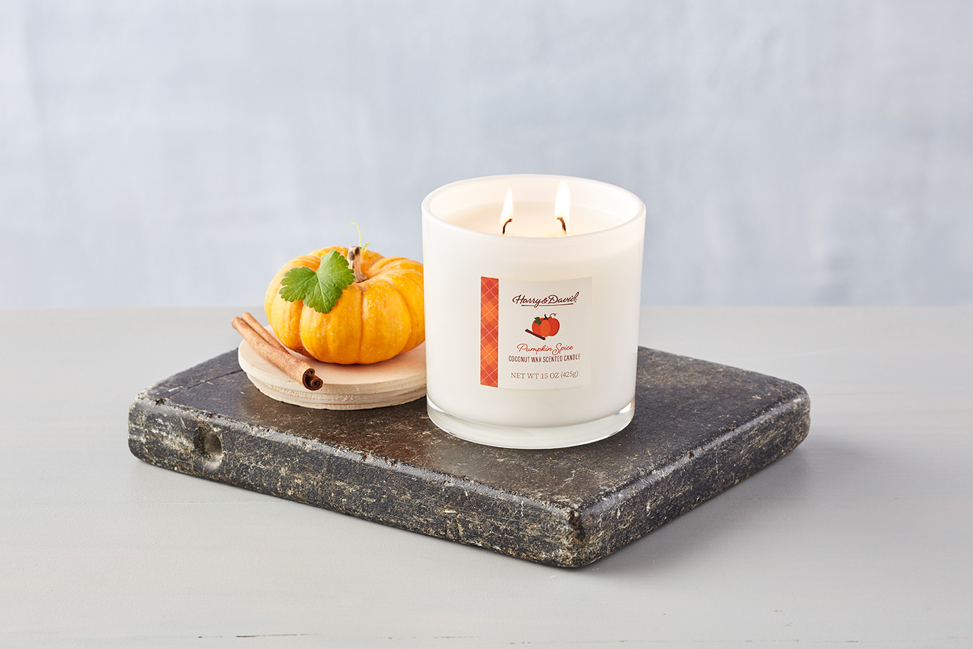 A lit pumpkin spice scented candle from Harry and David next to a mini pumpkin