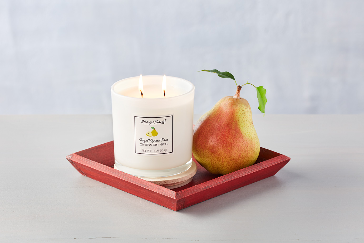 A lit pear scented candle from Harry and David next to a pear on a red tray