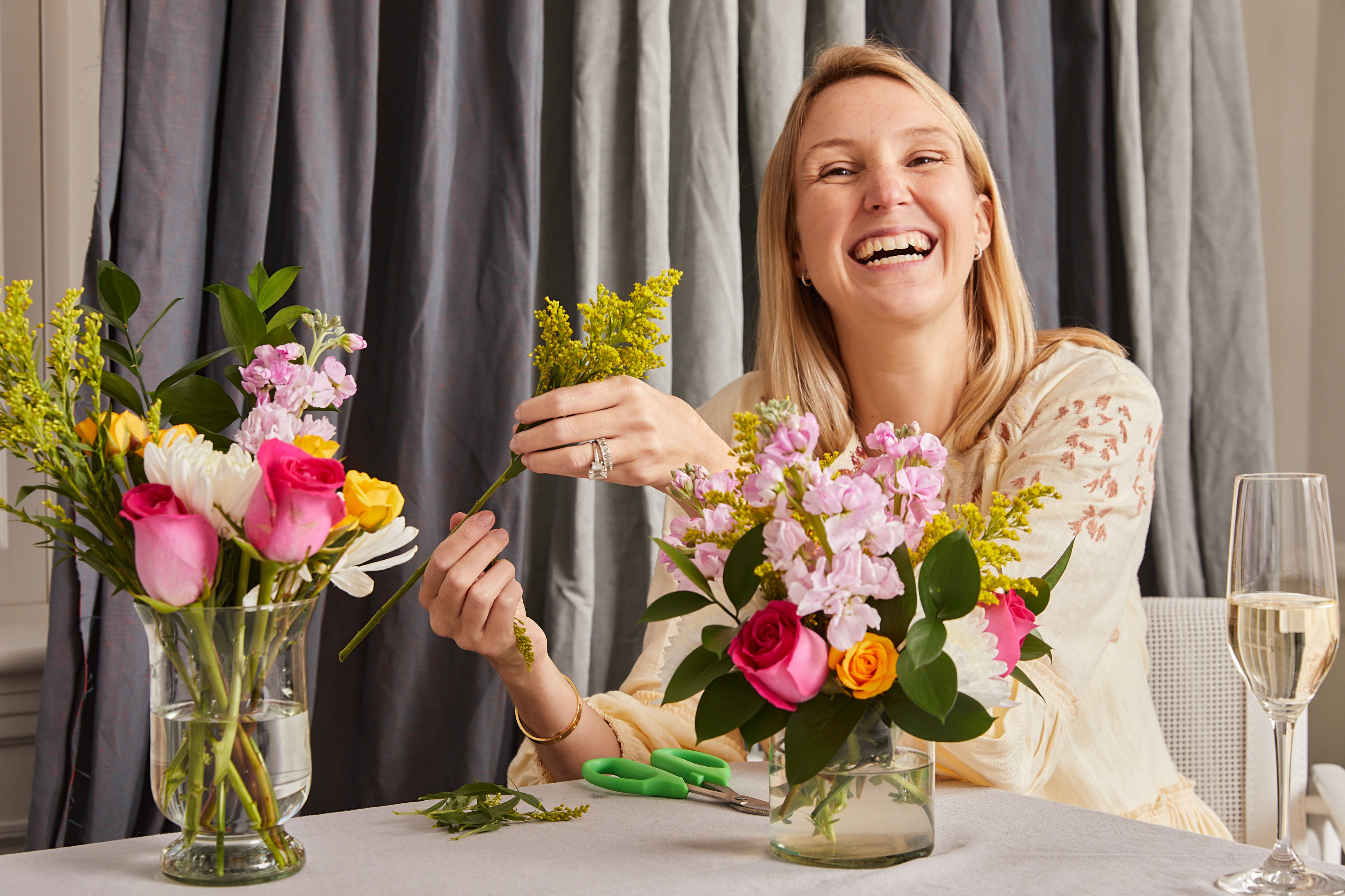 Alice from Alice's Table creating a bouquet of mixed, vibrant flowers next to a glass of champagne