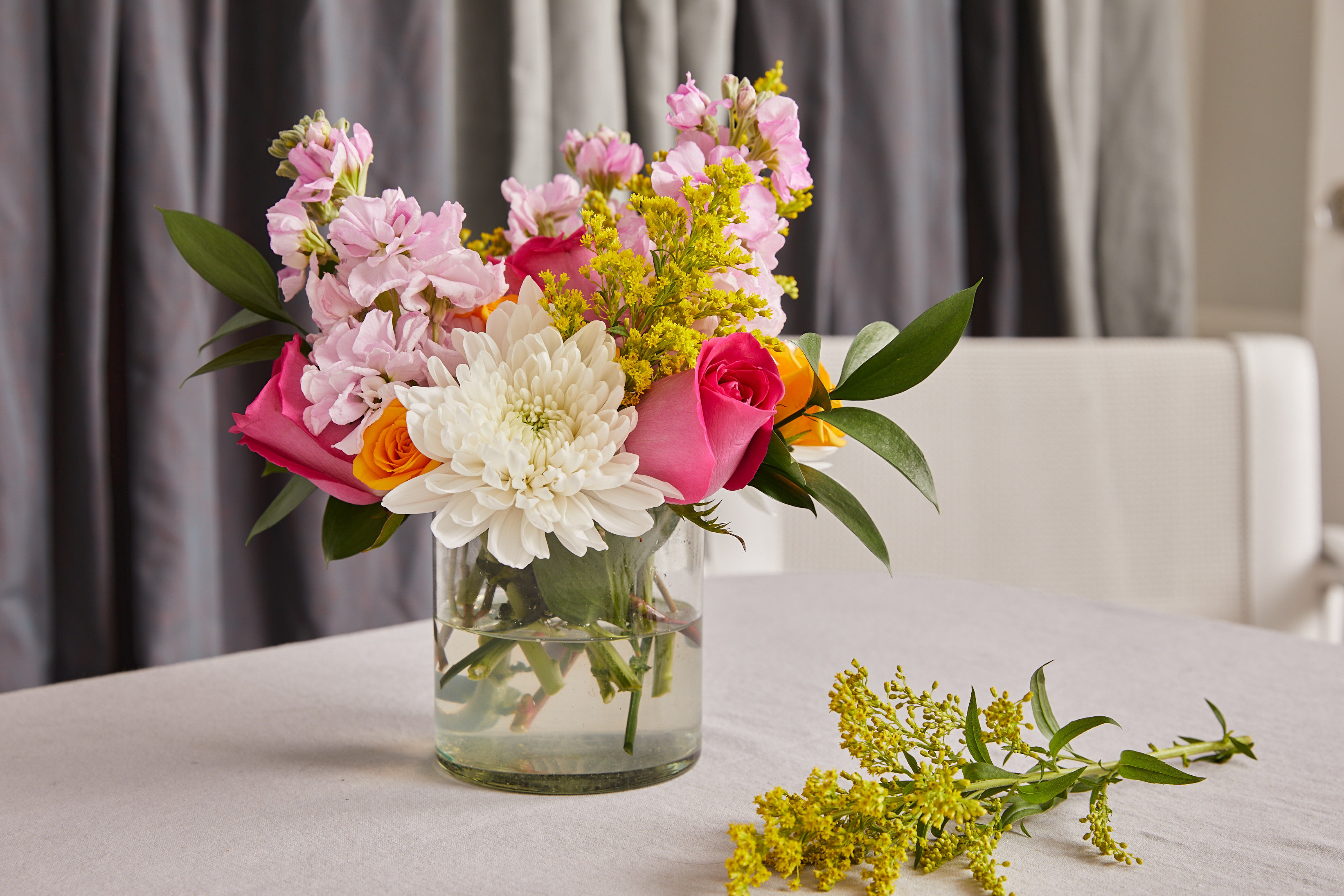A pink, orange, yellow, and white bouquet in a glass vase on a white linen table