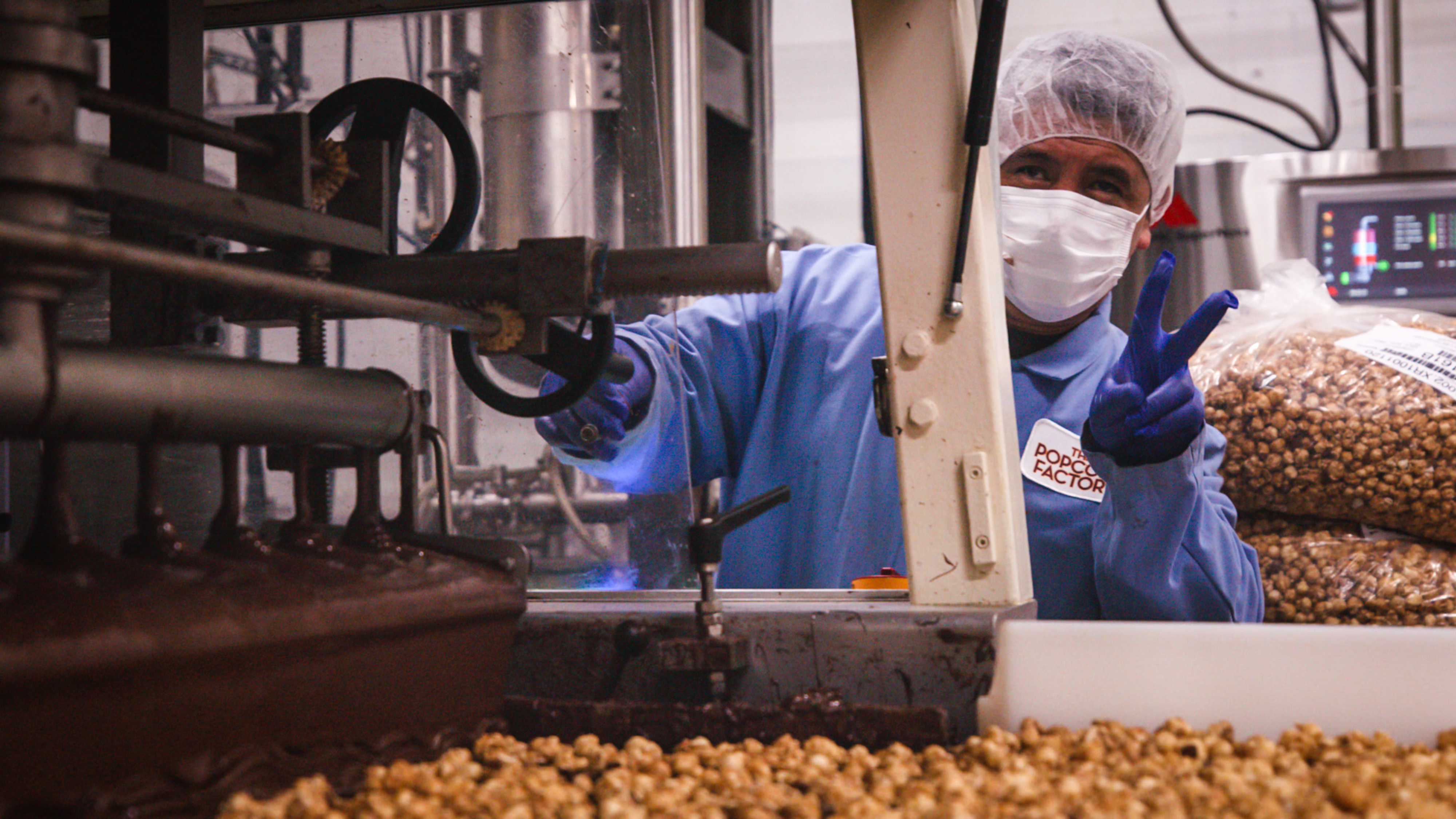 An employee at The Popcorn Factory making a peace sign while adding chocolate to the popcorn