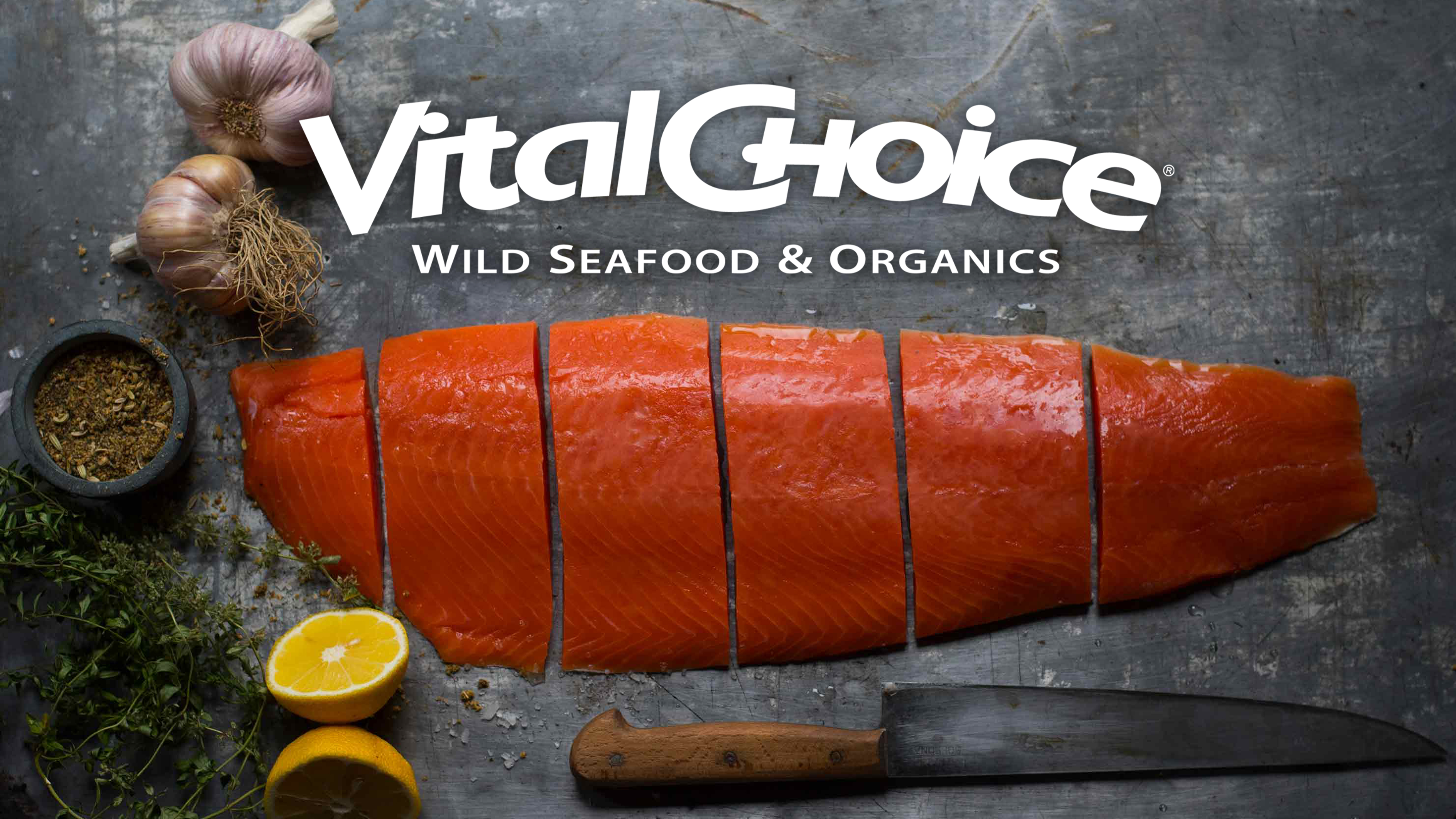 Salmon cut on a board next to herbs and lemon under the Vital Choice logo