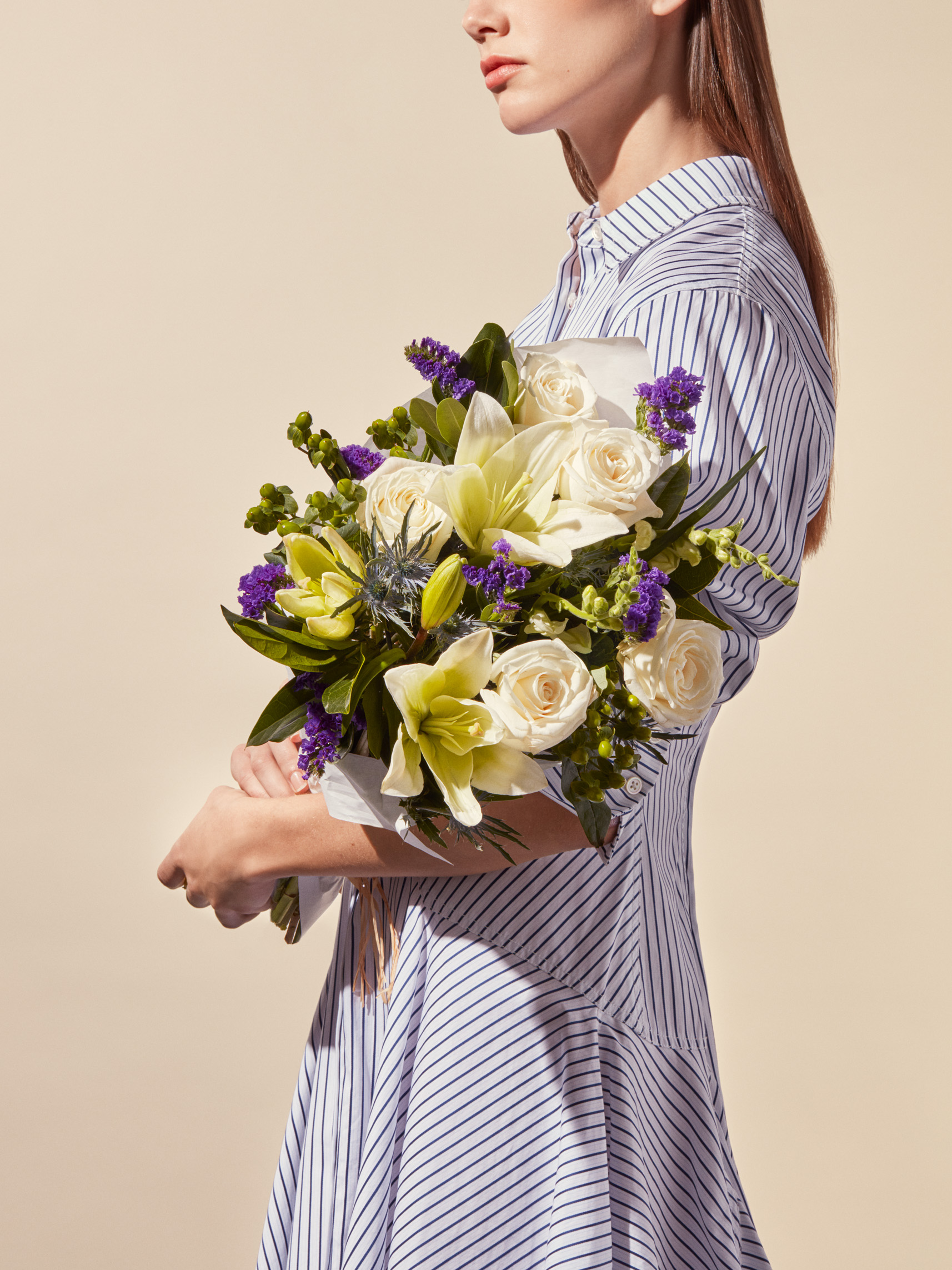 A woman in a striped dress holding a white and purple Poplin Crème Bouquet, part of the Jason Wu for Wild Beauty collection