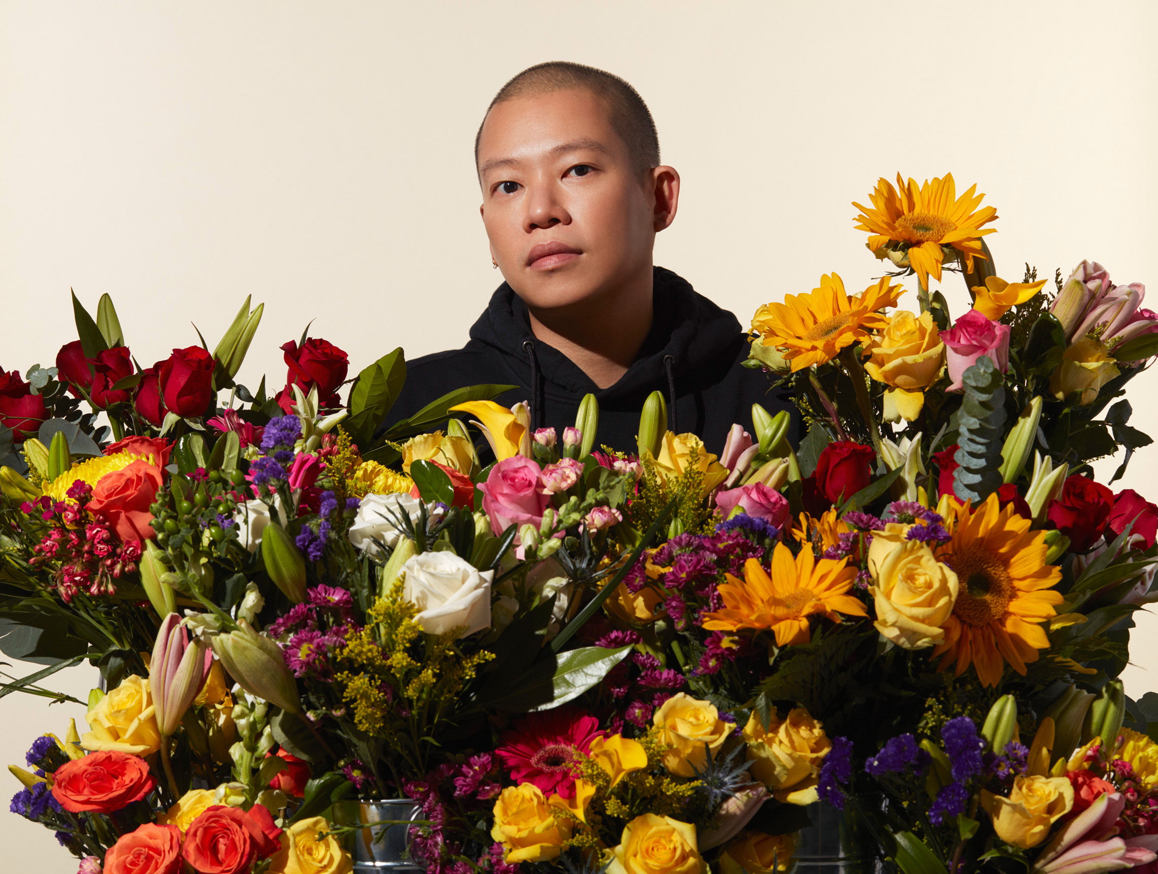 Designer Jason Wu standing behind a large display multi-colored floral bouquets