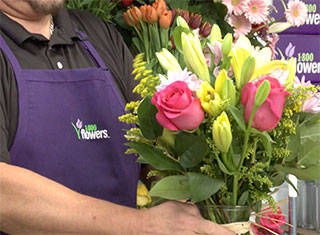 A 1-800-Flowers.com florist holding a colorful bouquet in a vase