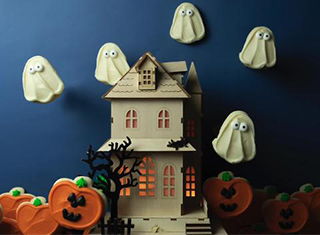 An assortment of Cheryl's Cookiesdecorated for Halloween surrounding a white wooden house