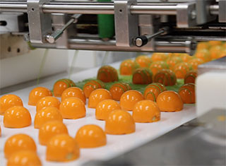 Orange covered chocolates on a conveyor in the Harry and David candy kitchen with green drizzling being added 