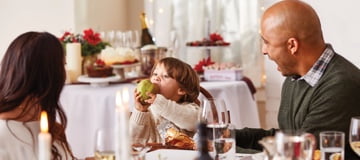 A child eating a pear from Harry & David with two adults as they sit a well decorated table