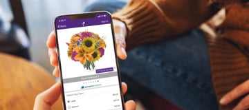 A smartphone with the 1-800-Flowers.com app on screen showing a bouquet in 3D