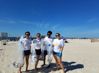 A group of volunteers posing with bags of trash during a beach clean up on a sunny day as a part of the 1-800-flowers.com Inc  Summer of a Million Smiles program