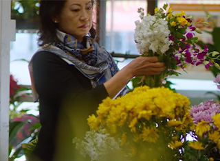 A BloomNet florist gathering a bouquet of purple, yellow, and white flowers