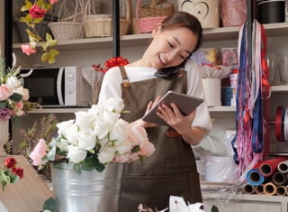 A smiling florist on the phone and using a tablet in their shop