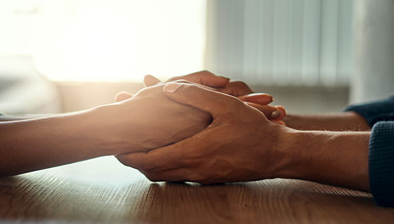 Two people holding hands across a table in a sunlit room