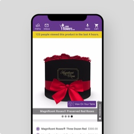 A smartphone with the 1-800-Flowers.com app AR and 3D visualization feature on screen showing the Magnificant Roses Preserved Roses product