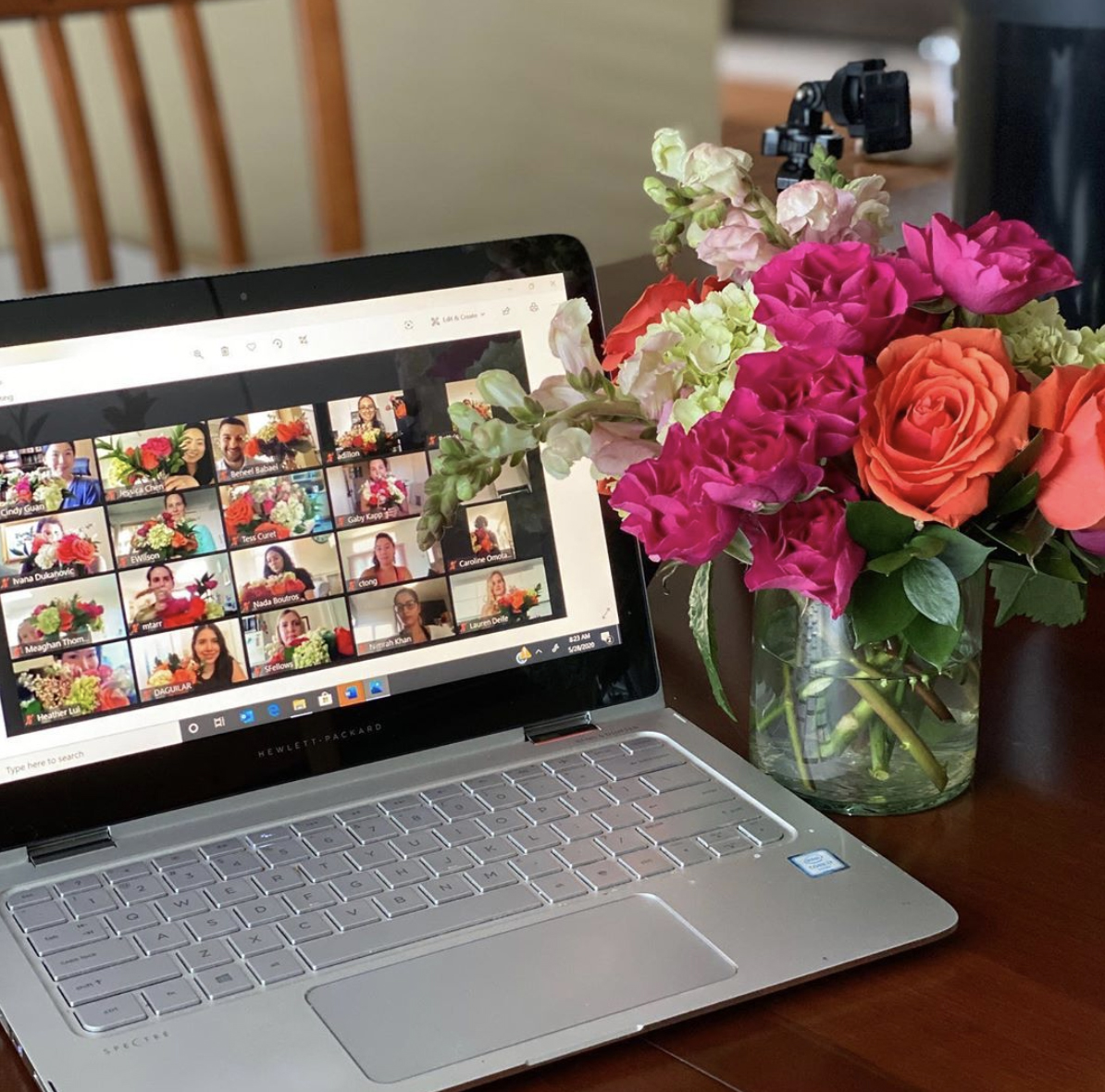 A laptop screen showing multiple people participating in an Alice's Table floral arranging workshop, next to a vibrant floral bouquet